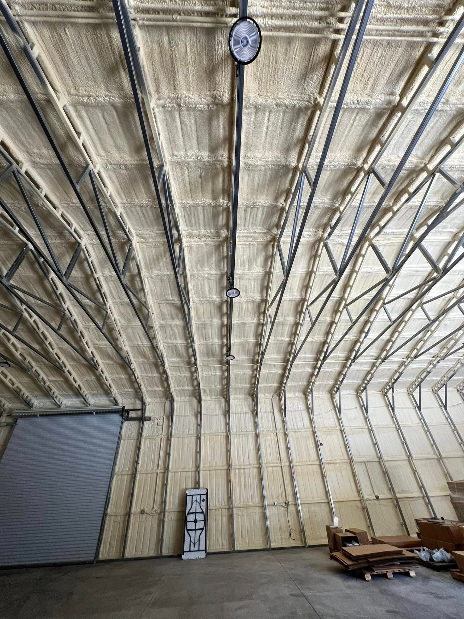 Interior view of an industrial building. Spray foam insulation covers the arched ceiling. A large door is on the left, and pallets are on the right.