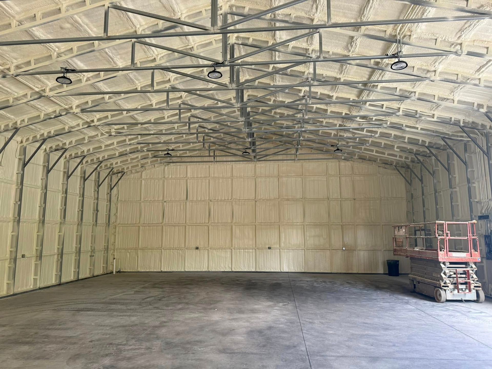 Interior of a large building with spray foam insulation on the walls and ceiling; concrete floor.