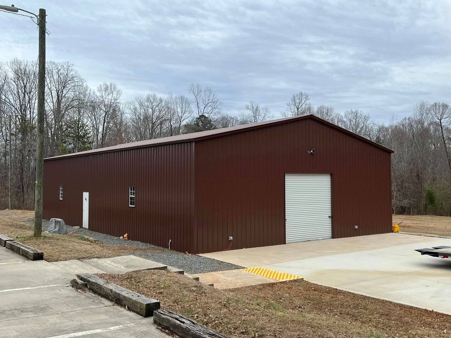 Brown metal building with a large garage door on a concrete slab; overcast sky.