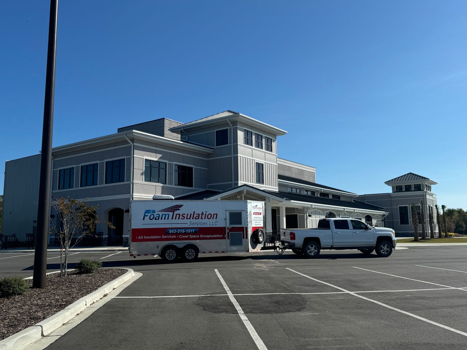 White truck pulling a trailer in front of a modern building on a sunny day. The trailer has a logo.