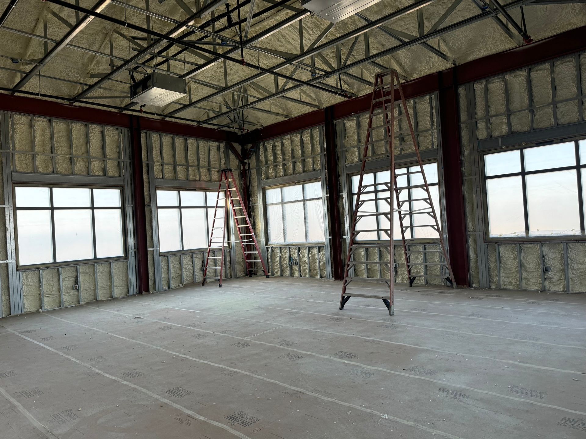 Interior of a building under construction, spray foam insulation, windows, ladders, unfinished floor.