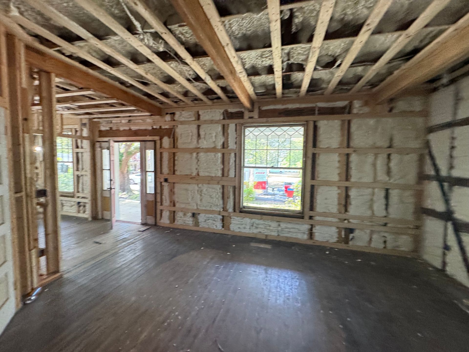Interior view of a room under construction, with exposed wooden beams, insulation, and framing.