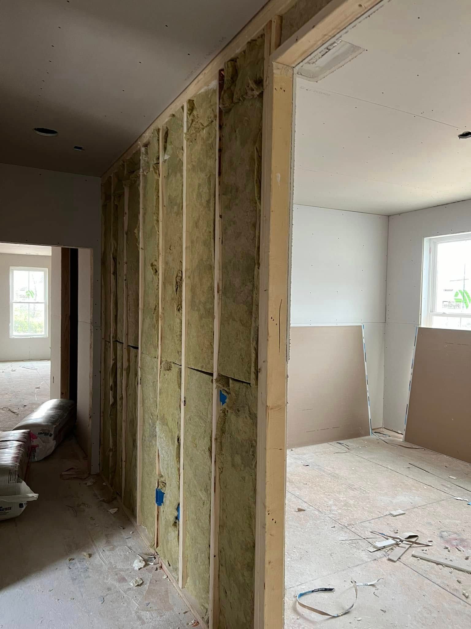 Interior view of a building under construction. Framed walls with insulation and a doorway. Drywall partially installed.