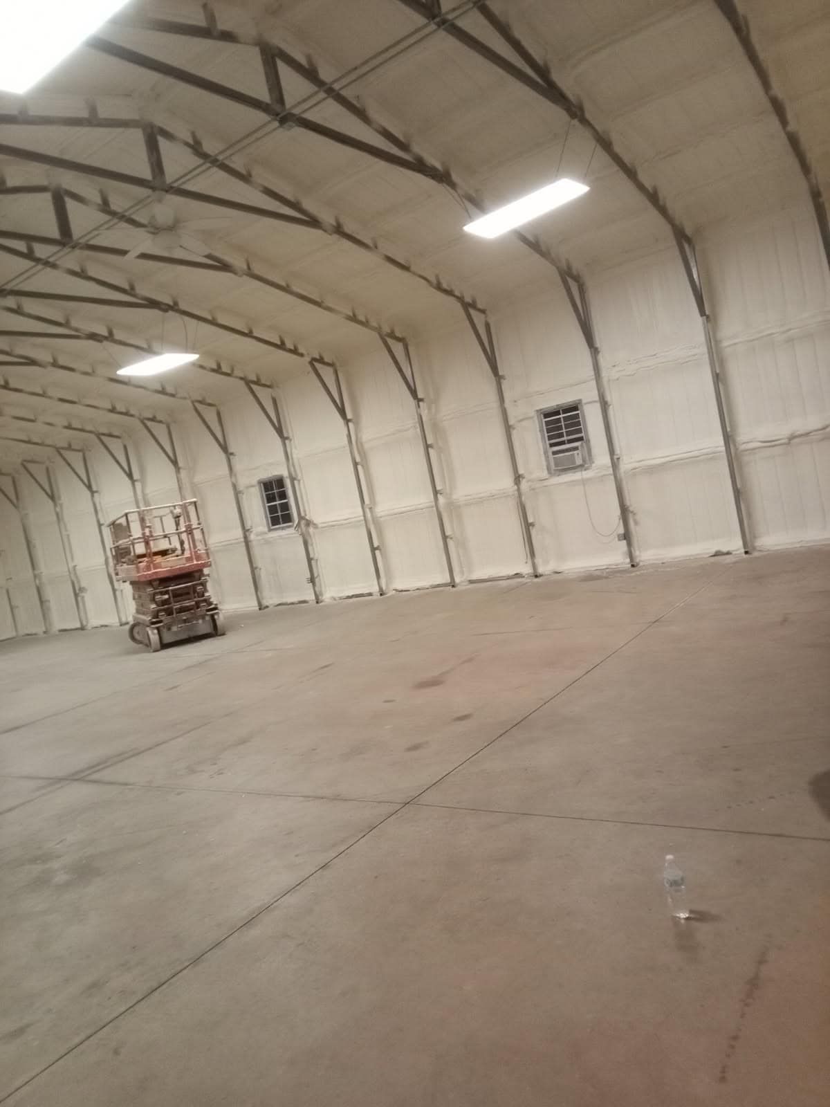 Interior of a large building, newly insulated with white spray foam. A lift is in the foreground.