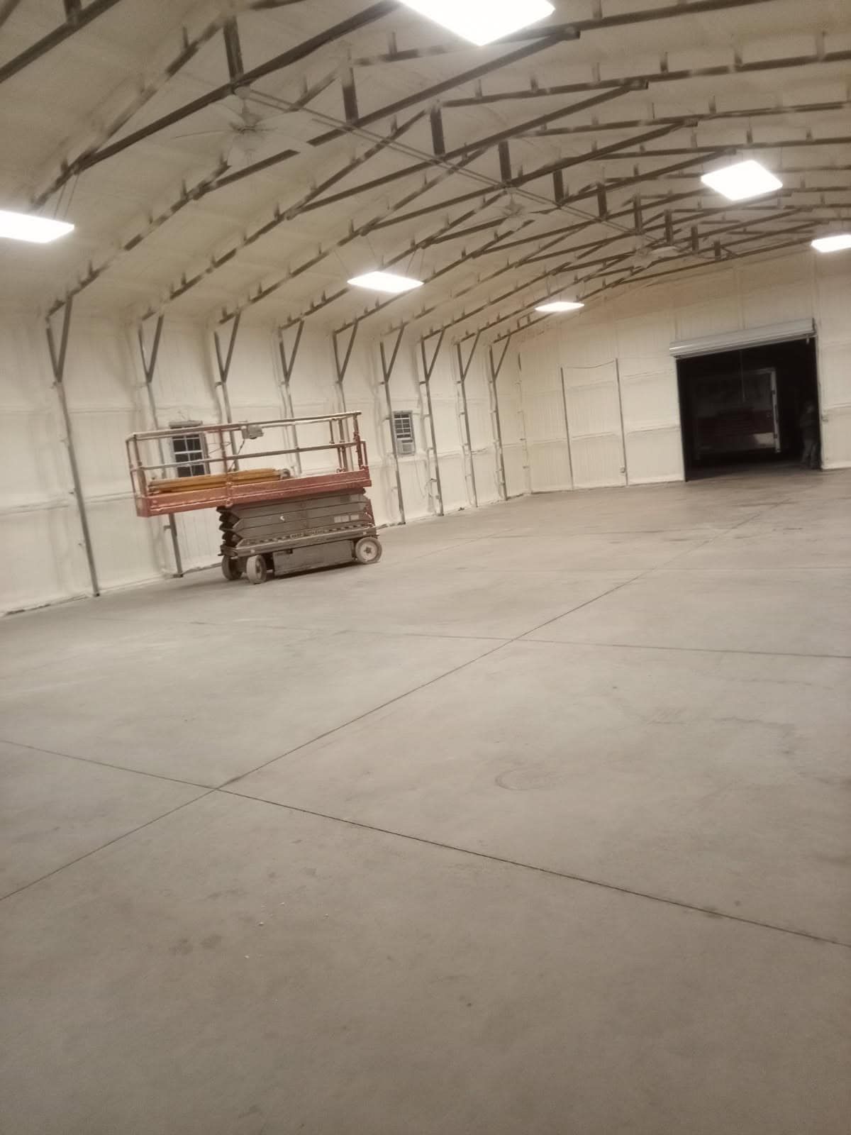 Large, empty warehouse interior. Spray foam insulation on walls, lift platform present.