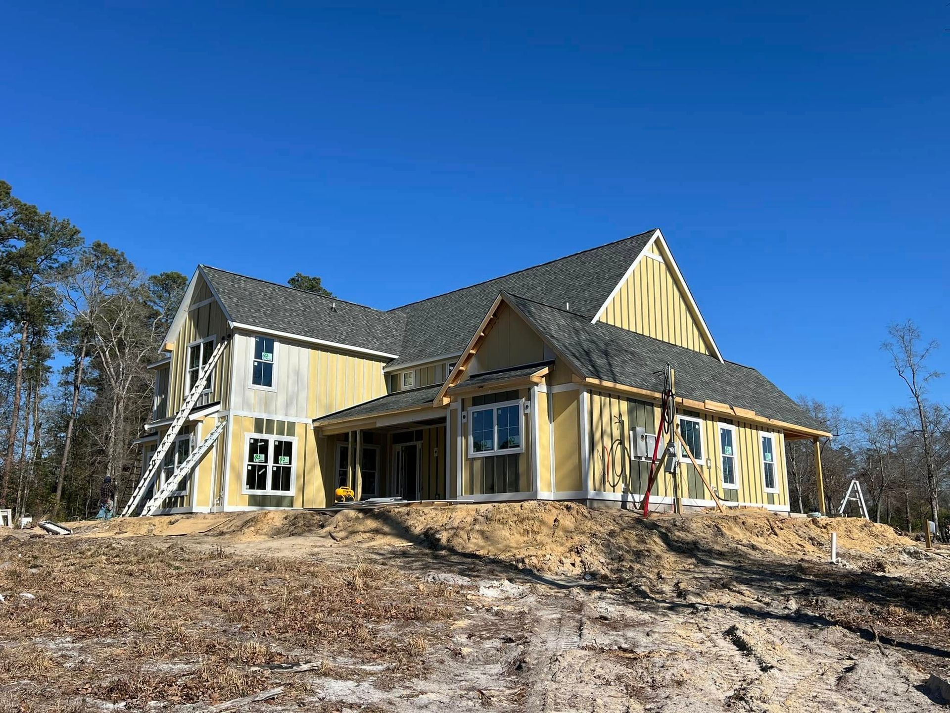 House under construction with yellow siding, gray roof, and blue sky.
