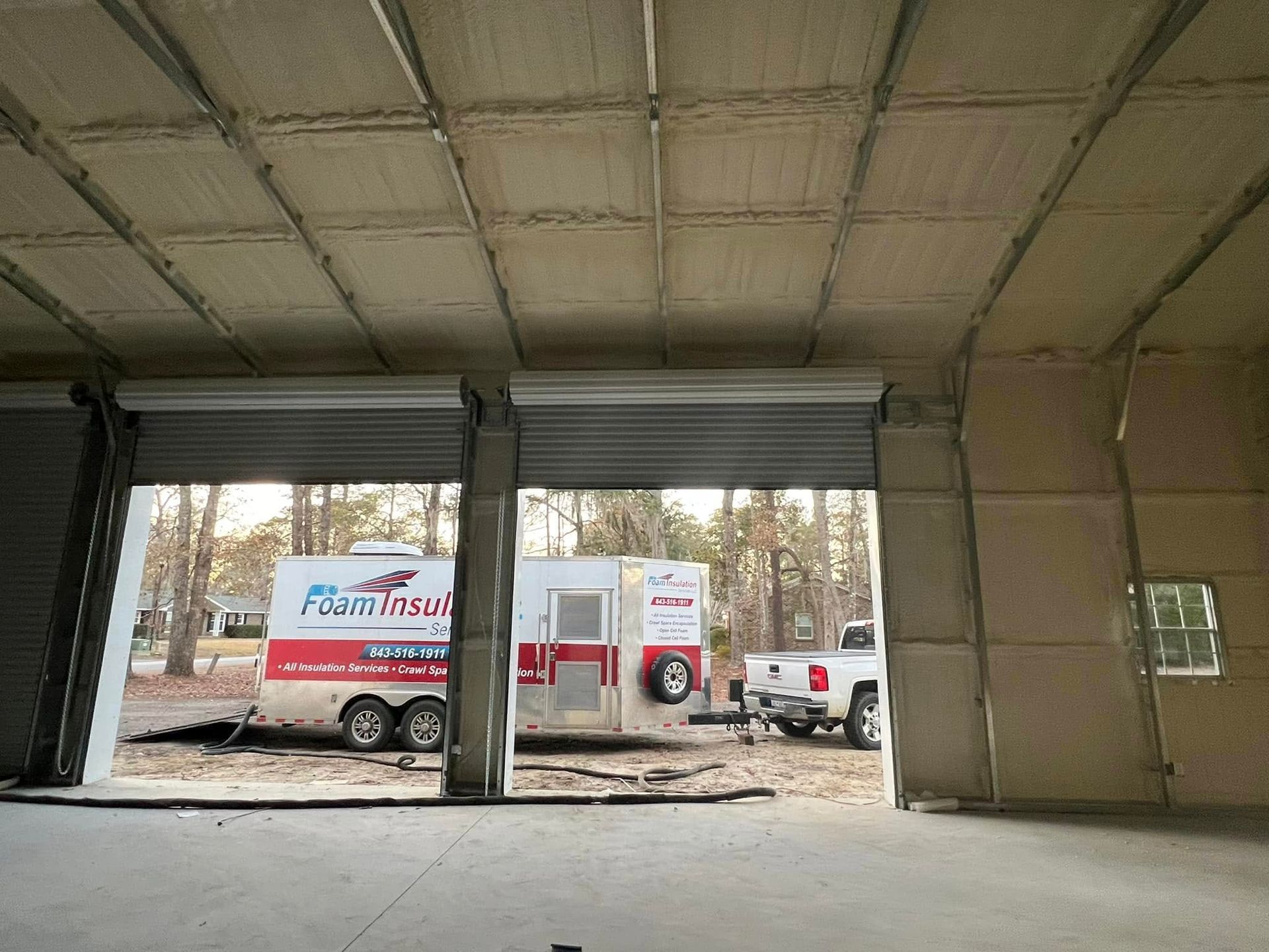 Interior view of a warehouse with roll-up doors open. Trailers and a truck are visible outside.