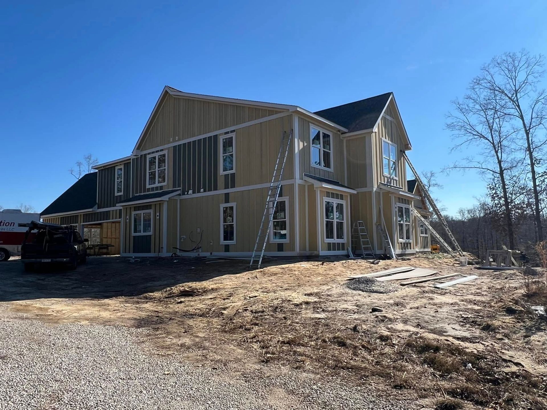 House under construction with tan and green siding; multiple ladders.