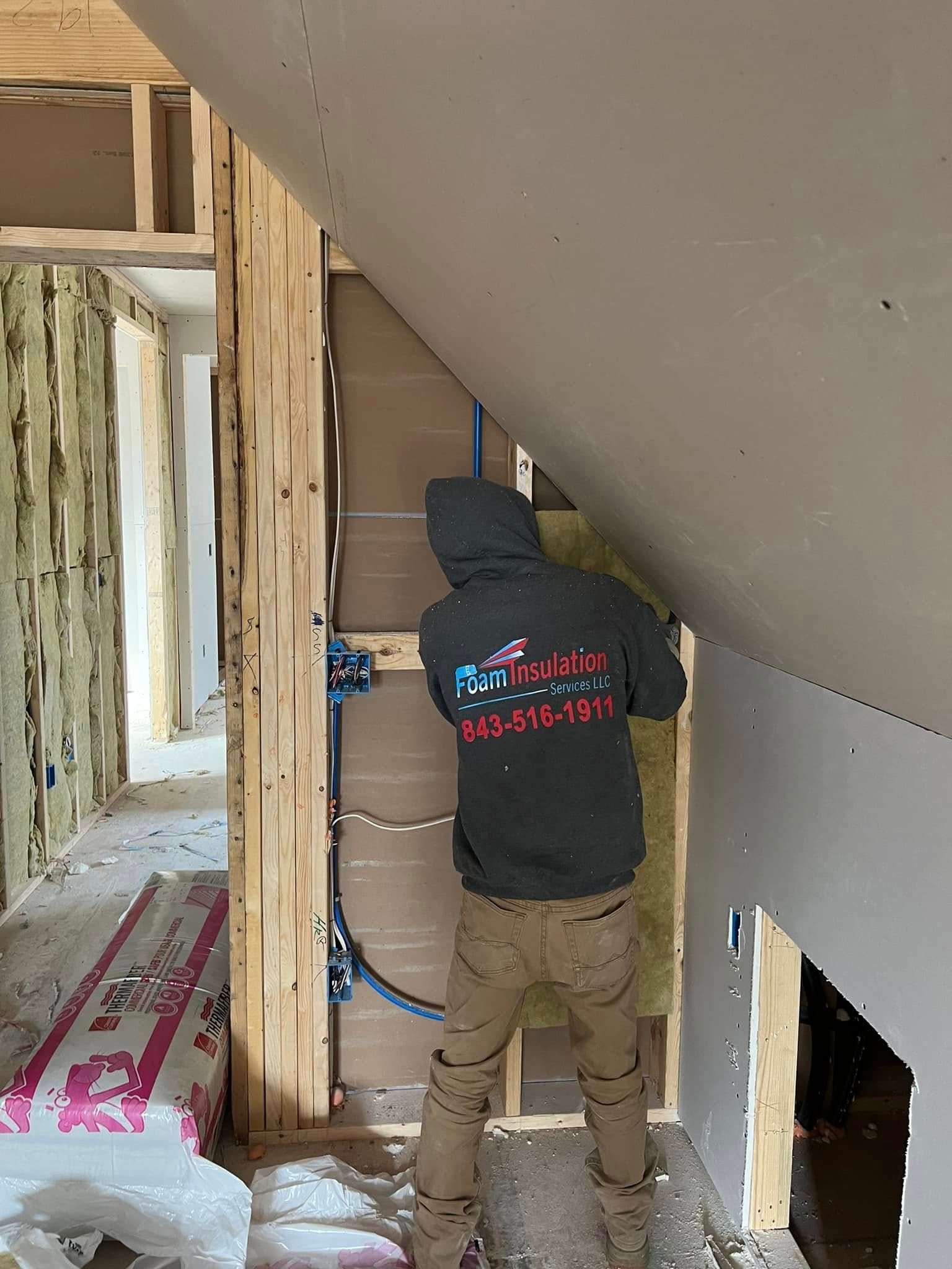 Construction worker insulating a wall; interior setting with drywall and electrical wiring.