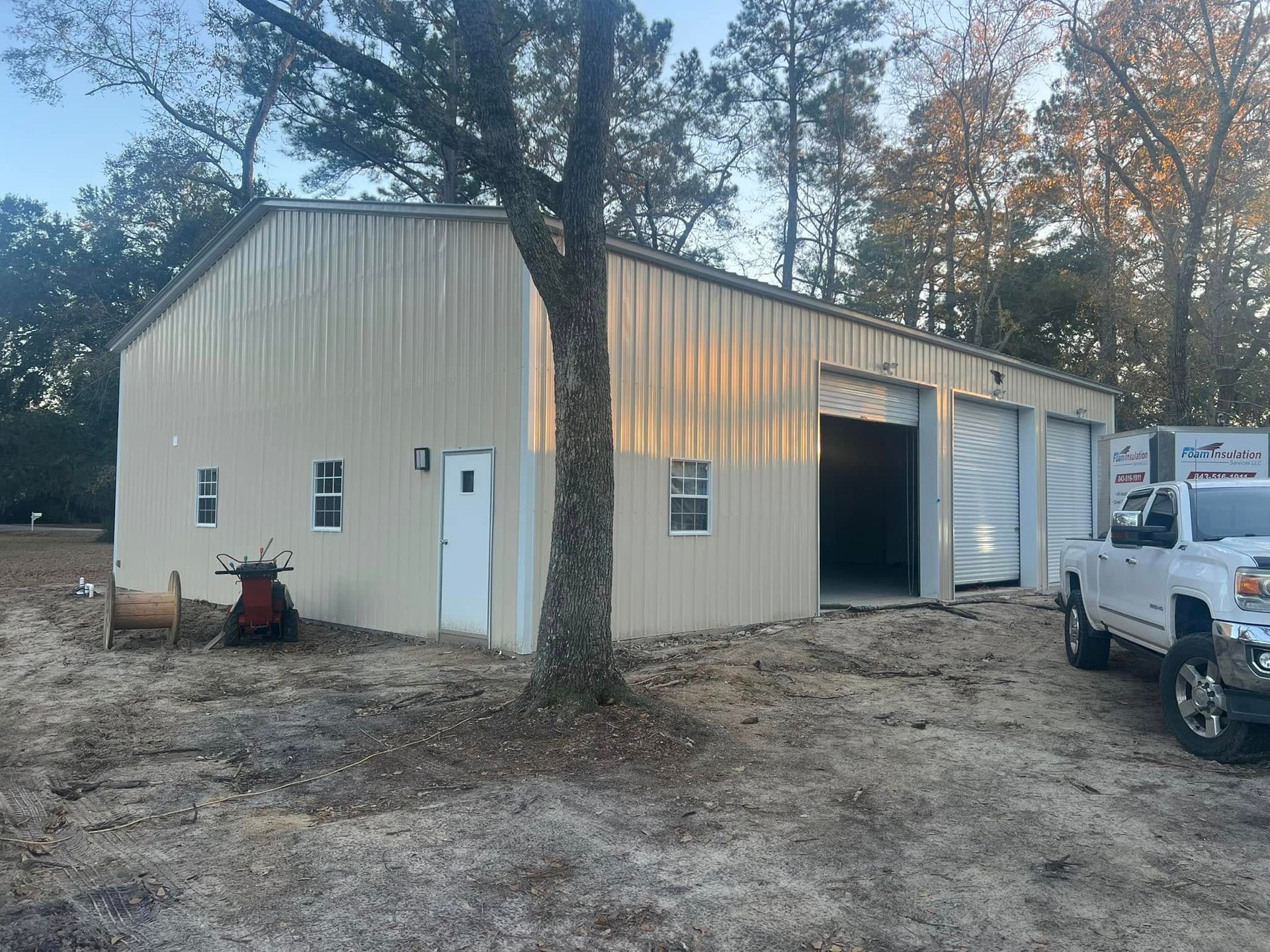 Tan metal workshop with open garage bay, white truck parked, tree in foreground.