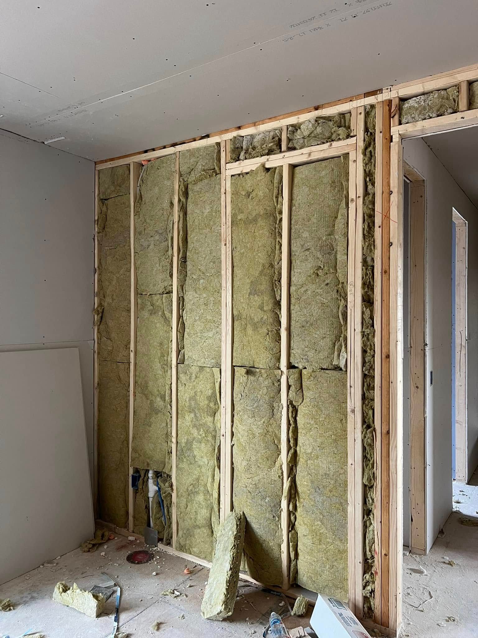 Interior wall under construction; wooden frame filled with insulation, drywall on ceiling, unfinished space.