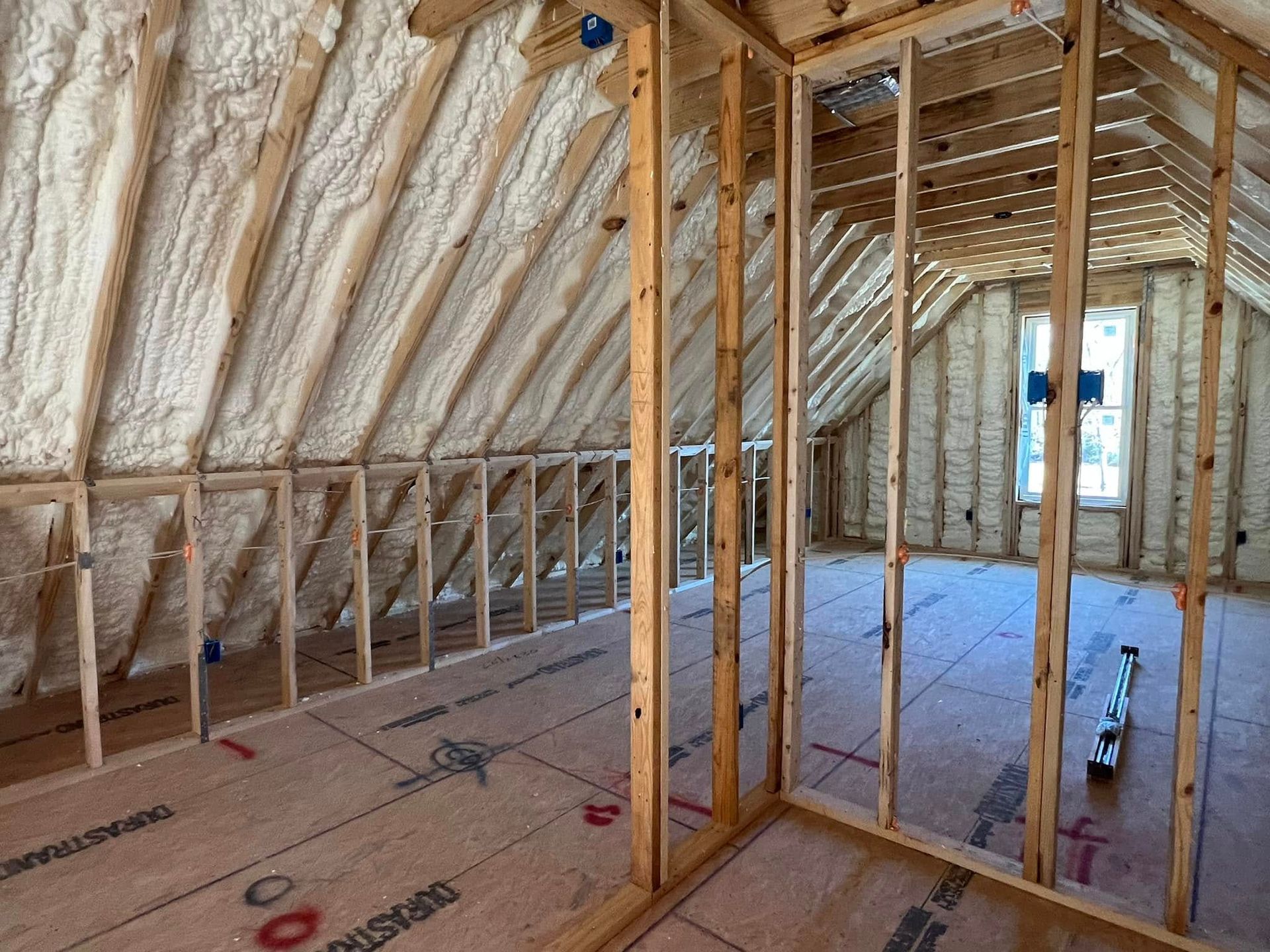 Interior view of a building under construction, featuring wooden framing and spray foam insulation.