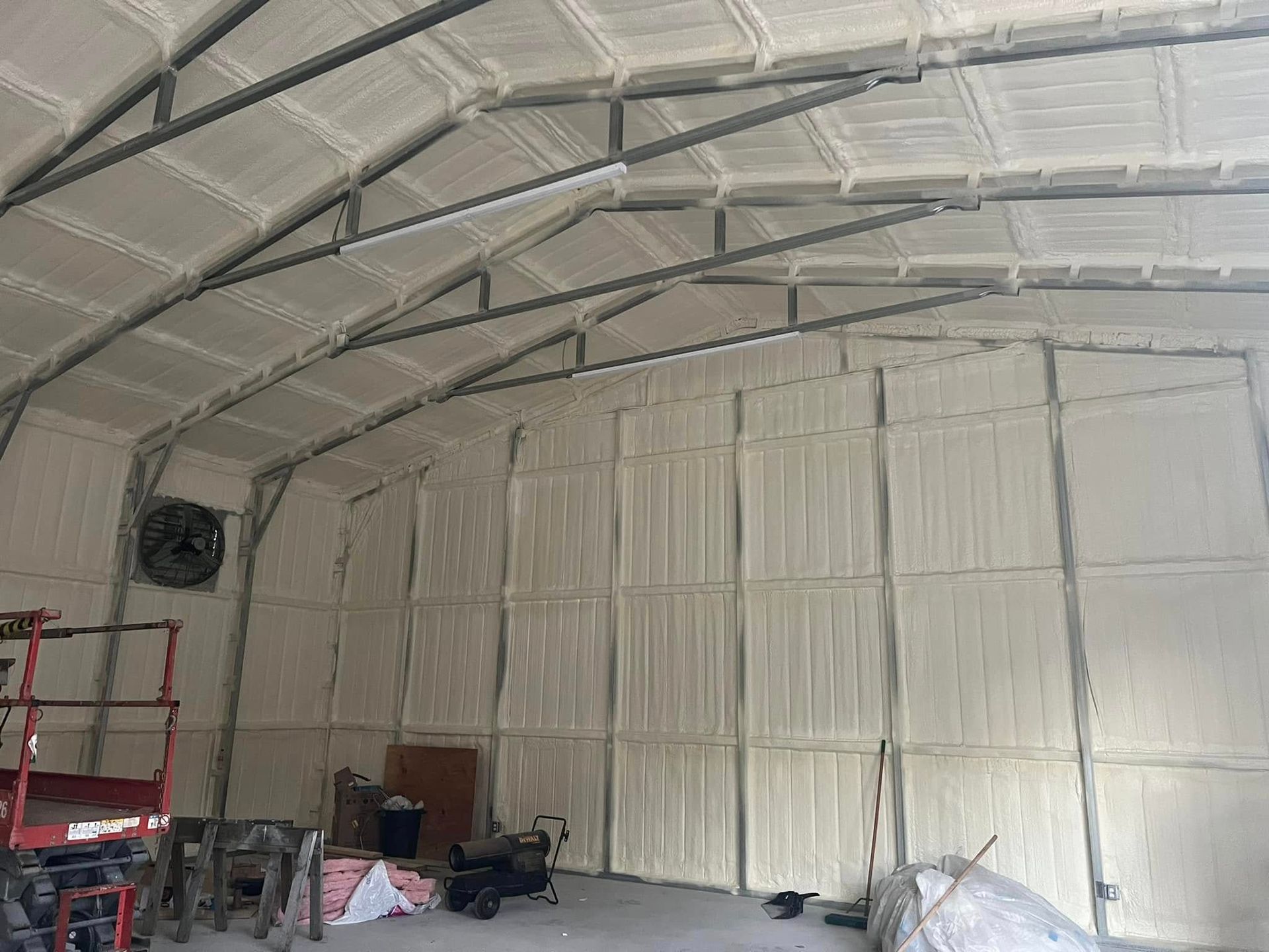 Interior of a building with white foam insulation on the walls and ceiling, metal beams support the structure.