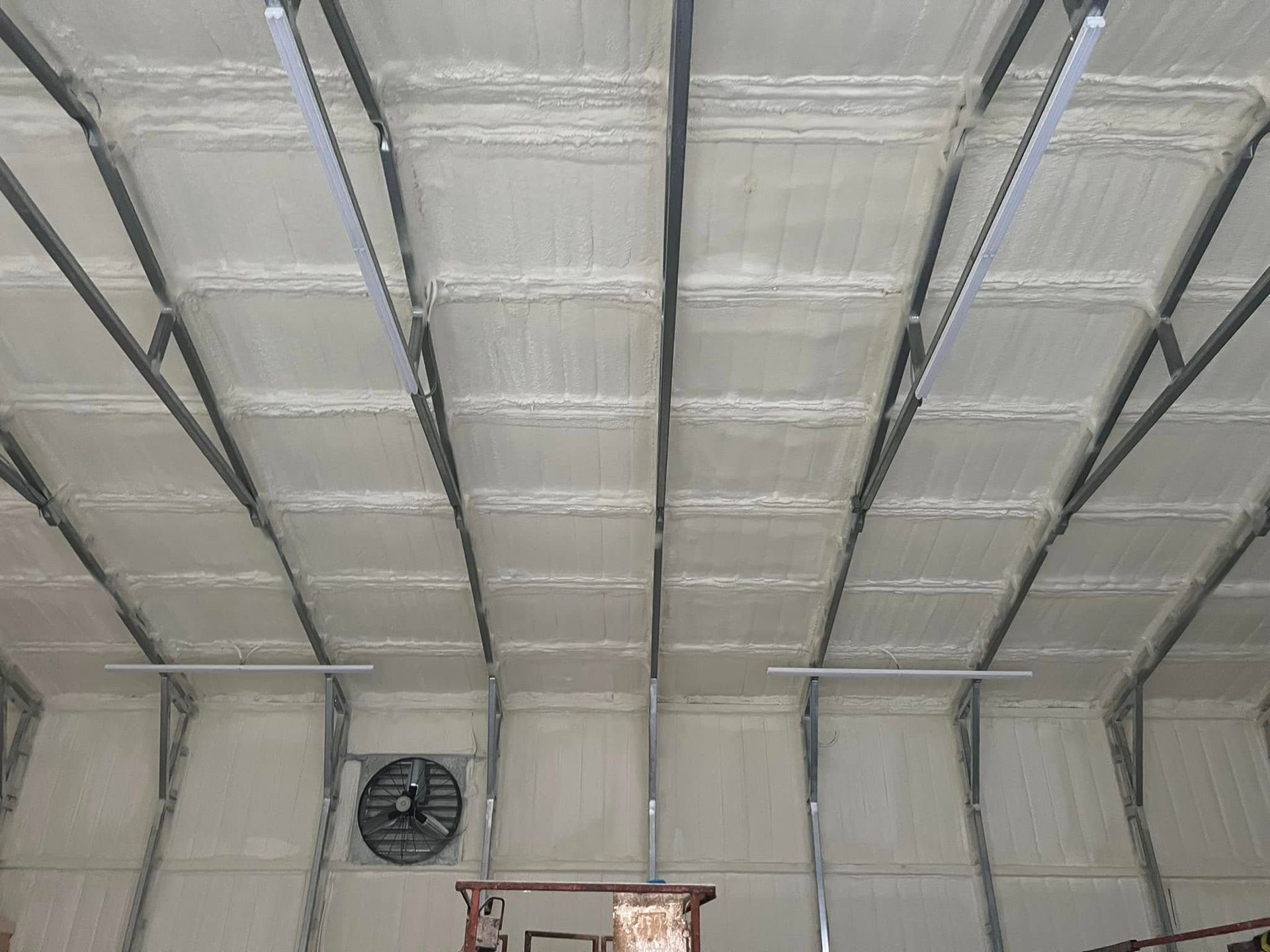 Insulated ceiling with white spray foam and gray metal supports in a building.