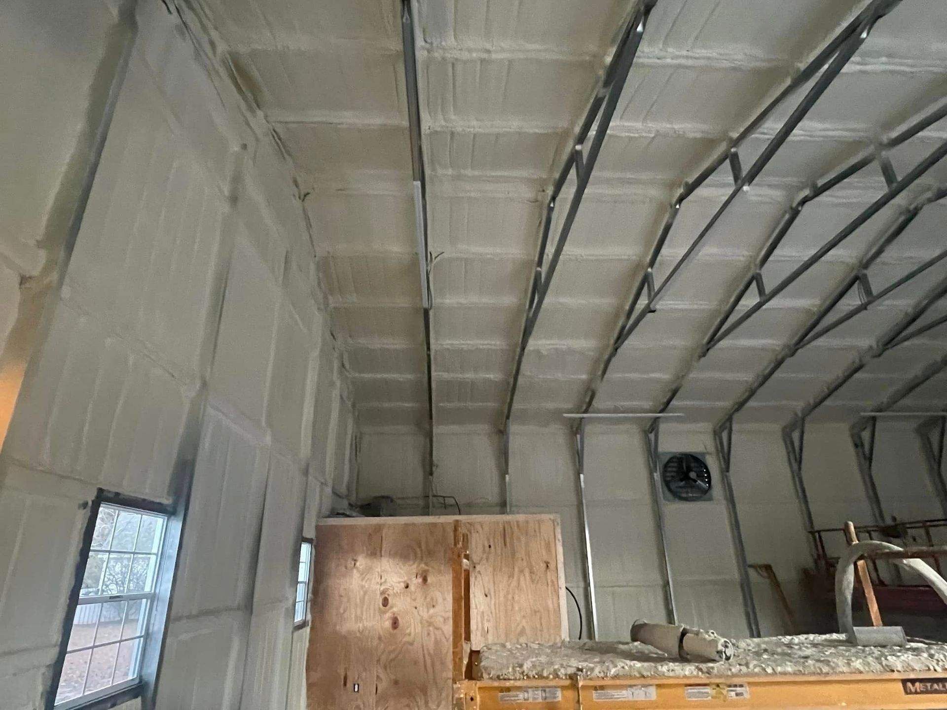 Interior view of a building insulated with white spray foam. Metal beams frame the curved ceiling and walls.