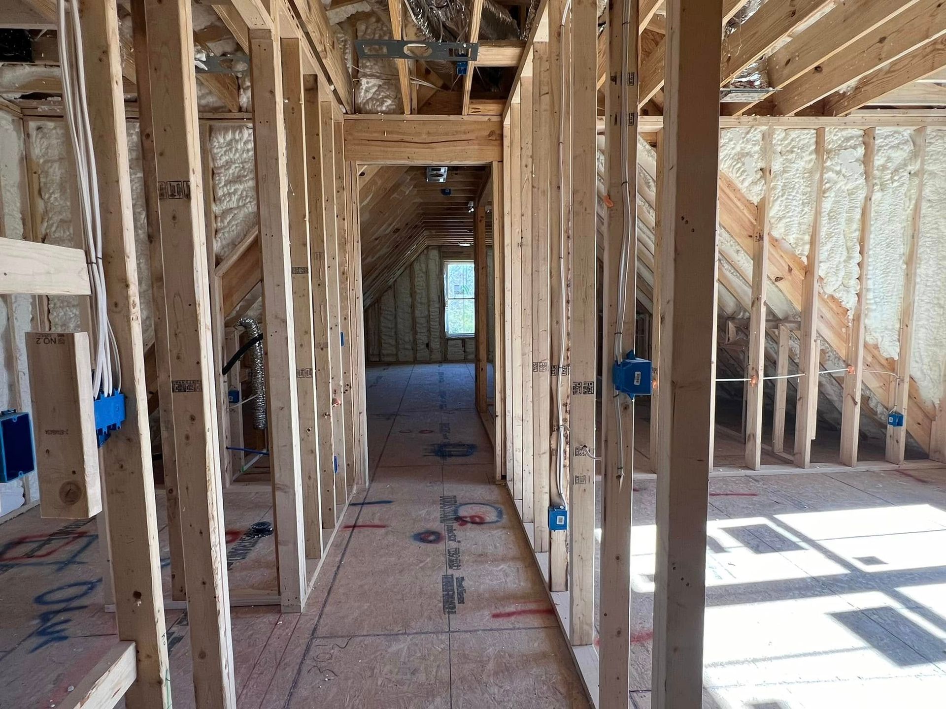 Interior view of a building under construction, showing wooden framing and spray foam insulation in the walls.