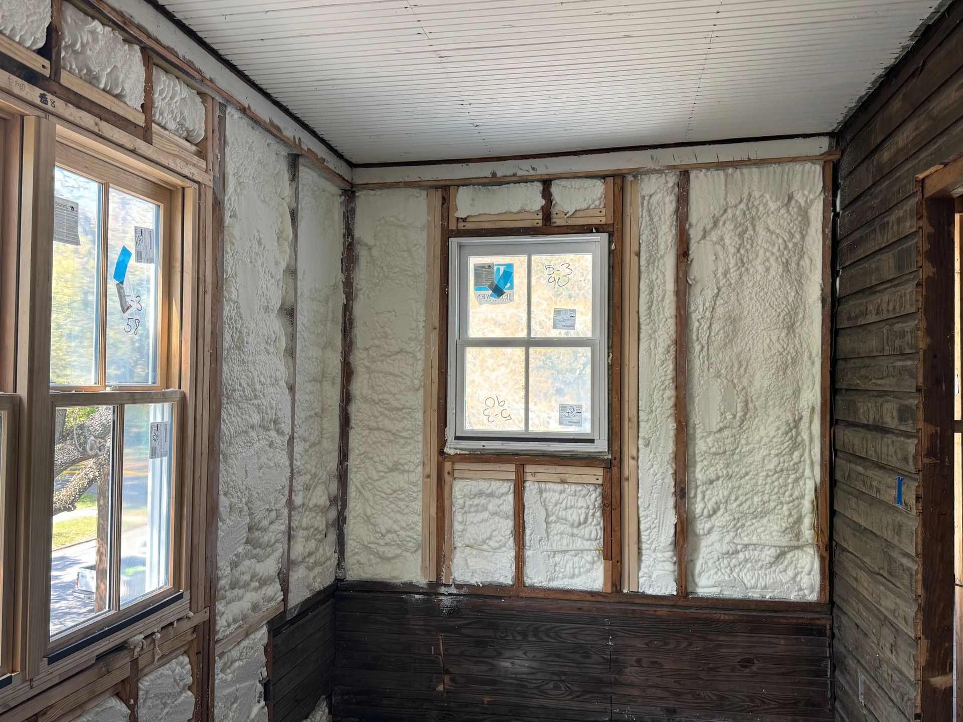 Interior room renovation; exposed wooden framing filled with white insulation foam around windows.