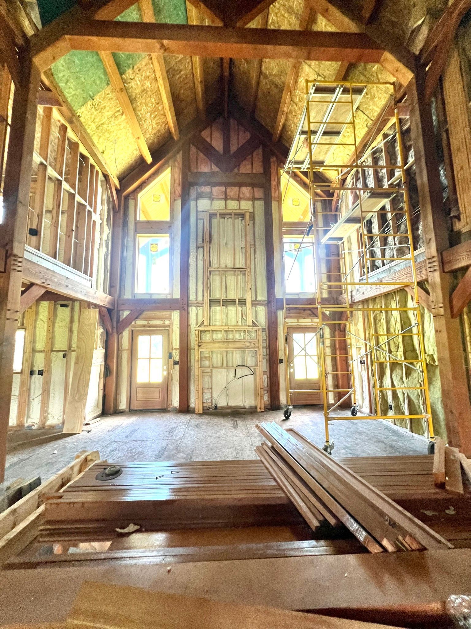 Interior of a house under construction; wooden beams and framing with insulation visible. Scaffolding in the room.