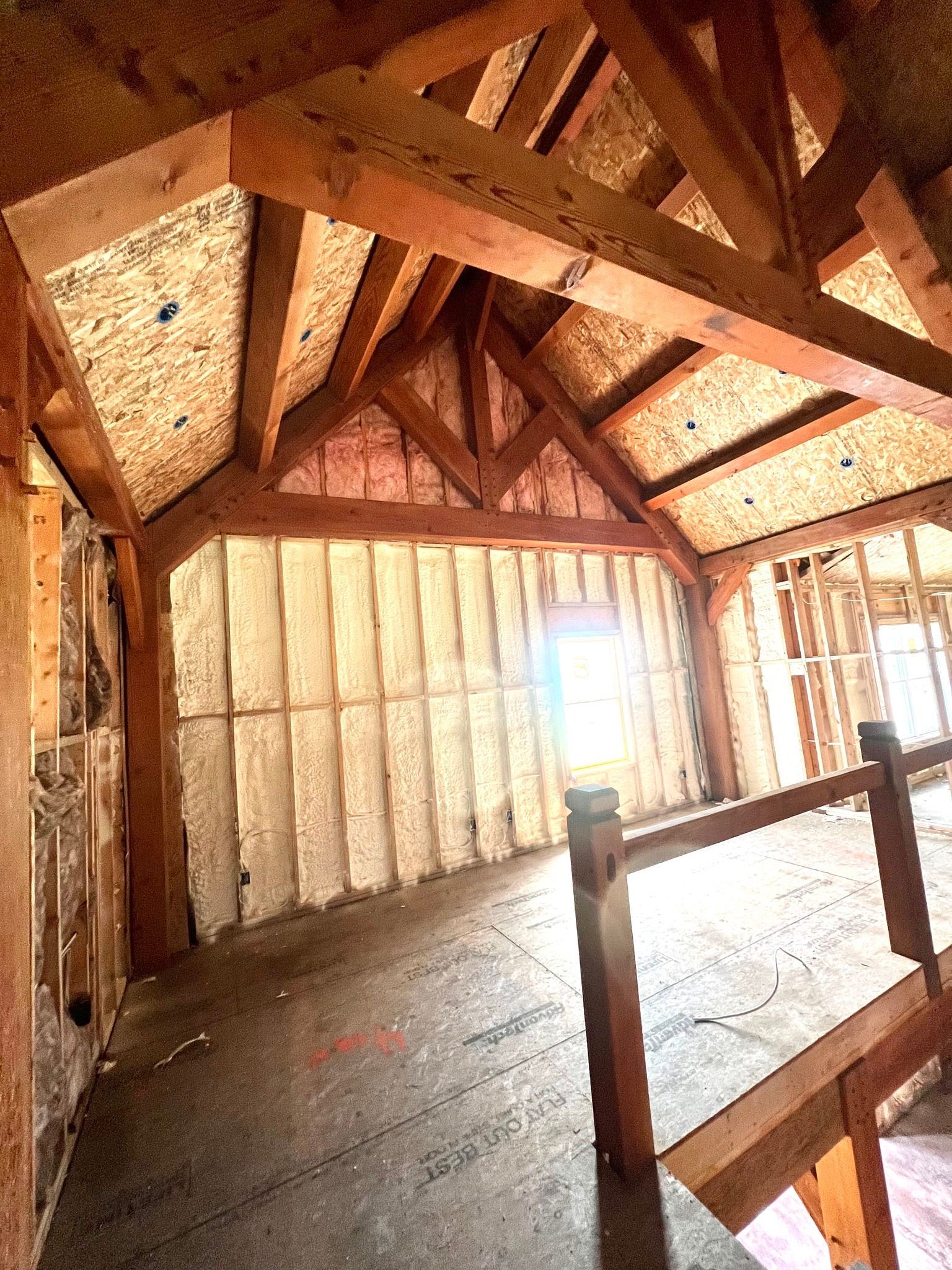 Interior of a building under construction, showing wooden beams, insulation, and an unfinished floor.