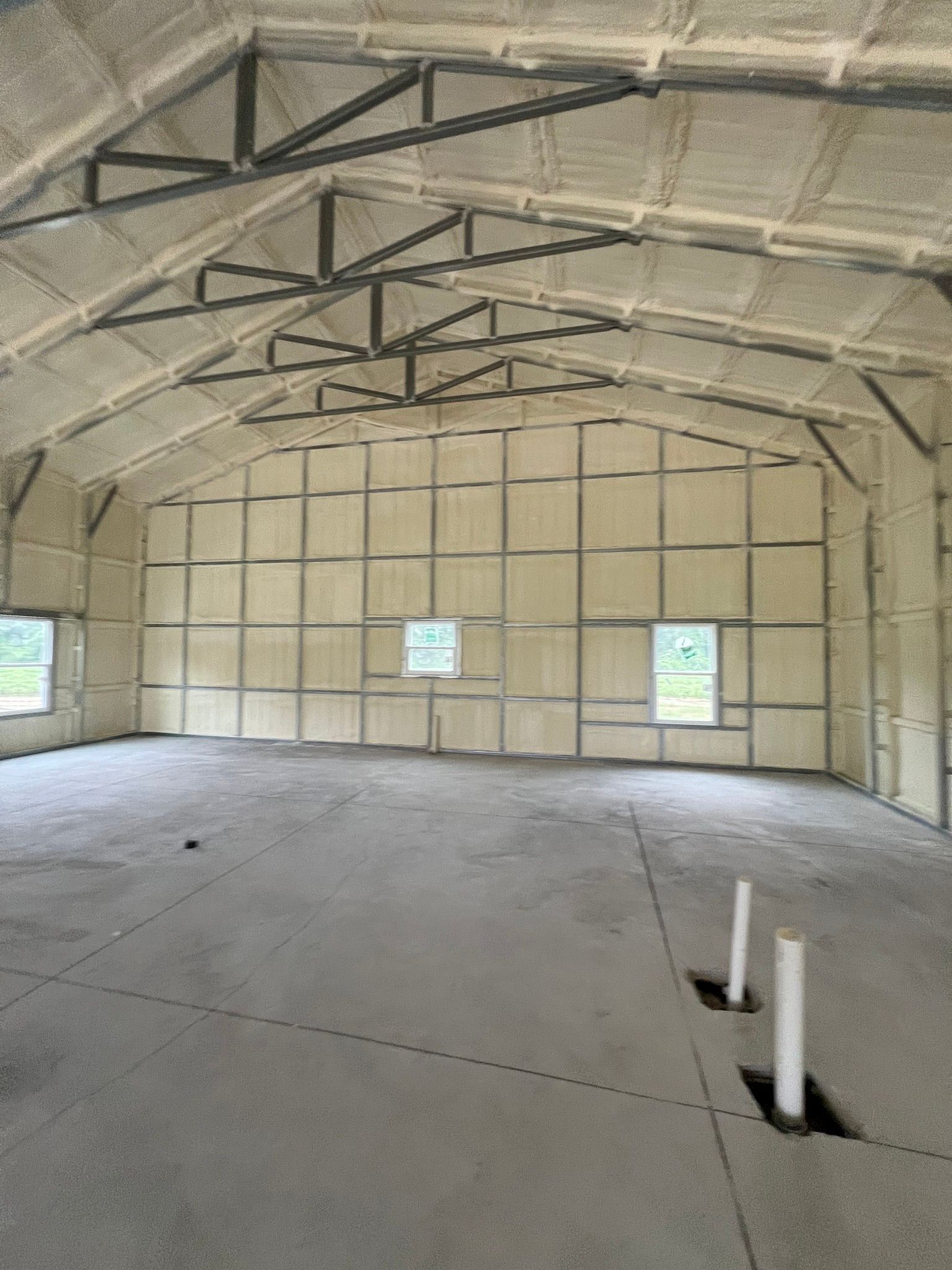 Interior view of a building with concrete floor and walls and ceiling covered in insulation.
