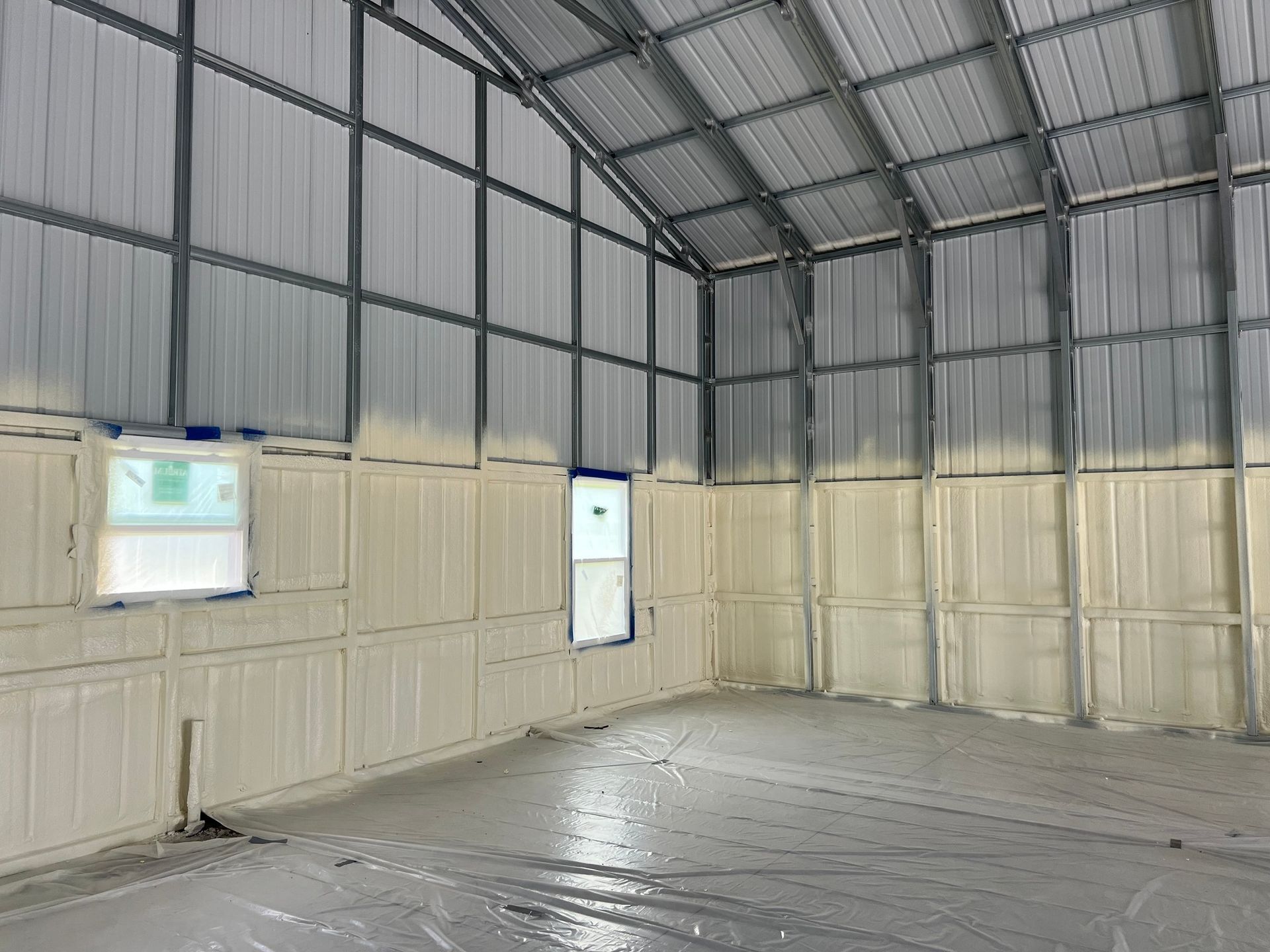 Interior of a metal building with spray foam insulation on walls. A window and door are visible.