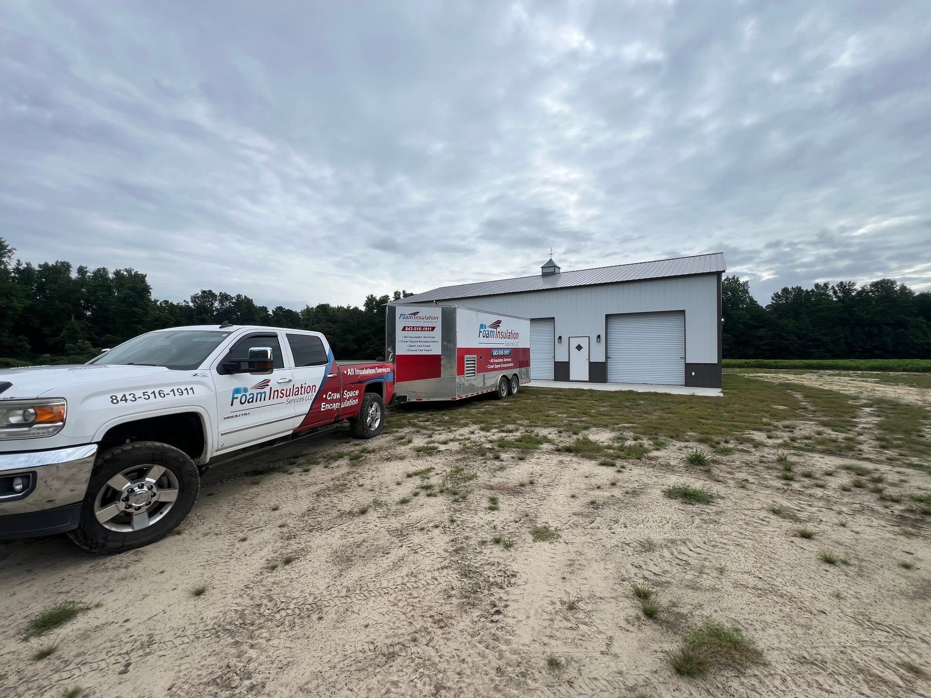 White pickup truck with trailer parked in front of a white building with a garage door on a cloudy day.