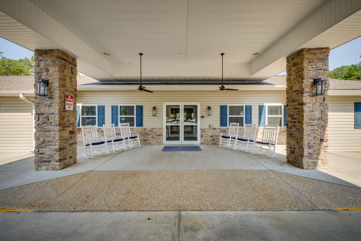A large building with a covered porch and chairs in front of it.