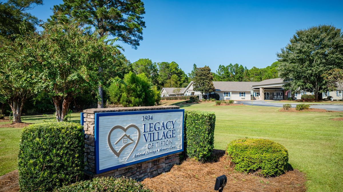 A sign for legacy village is sitting in the middle of a grassy field.