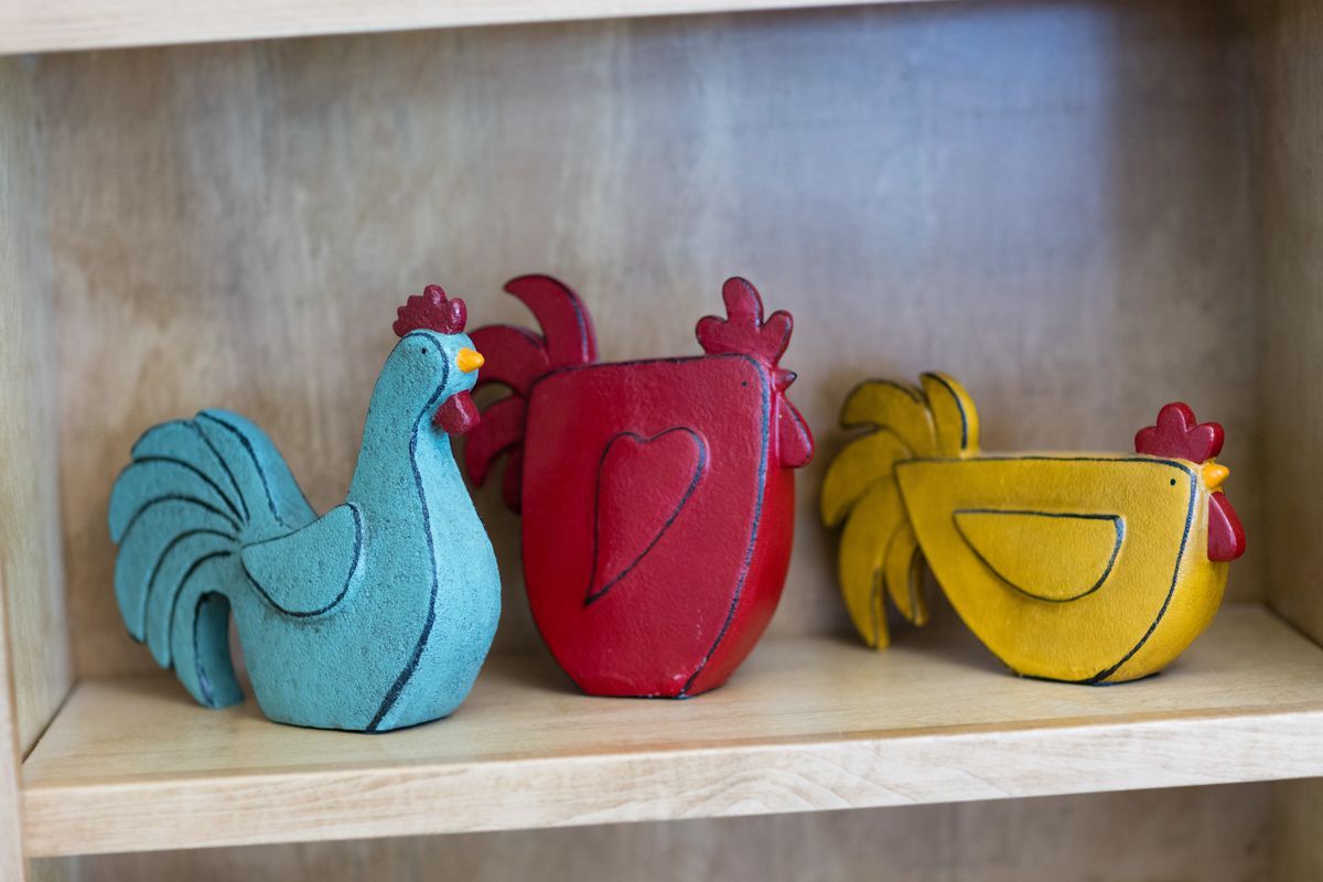 Three colorful roosters are sitting on a wooden shelf