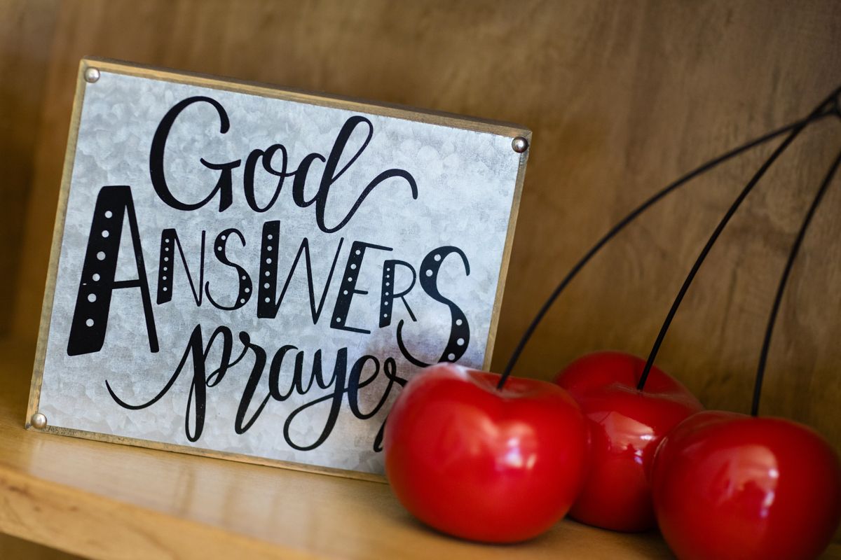 A sign that says `` god answers prayer '' is on a wooden shelf next to red apples.