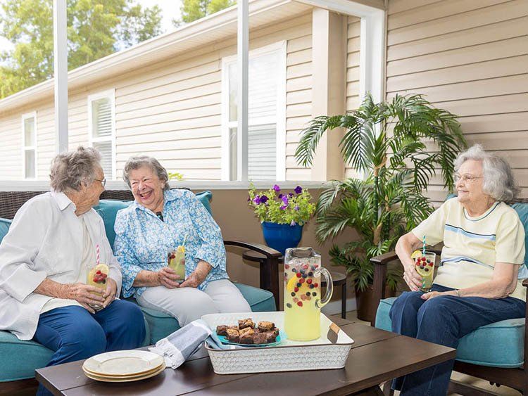 Three older women are sitting on a porch drinking lemonade.
