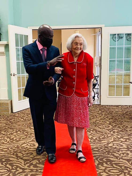 A man in a suit is helping an older woman walk down a red carpet.
