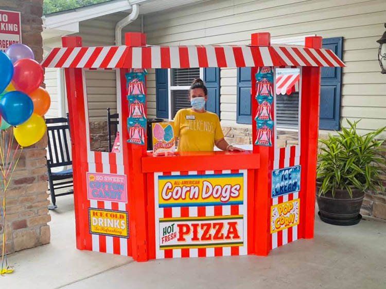 A woman wearing a mask stands behind a corn dogs and pizza stand