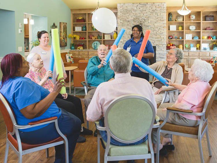 A group of elderly people are sitting in chairs playing with balloons.