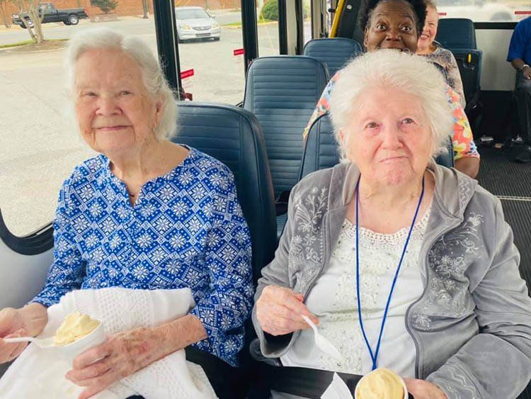 Two elderly women are sitting on a bus eating food.