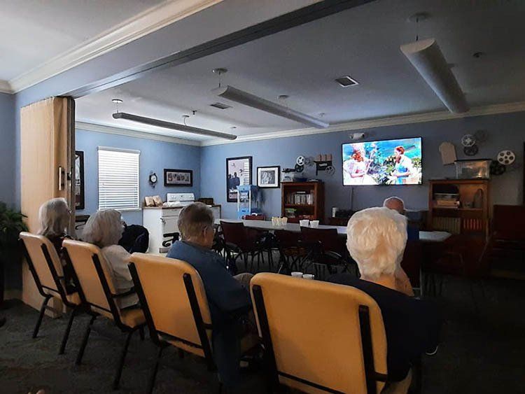 A group of people are sitting in chairs in a room watching a television.