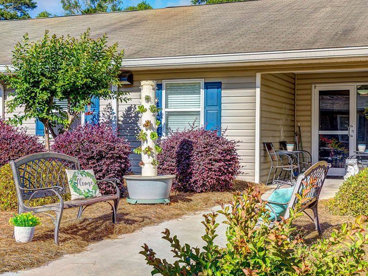A house with a bench and chairs in front of it.
