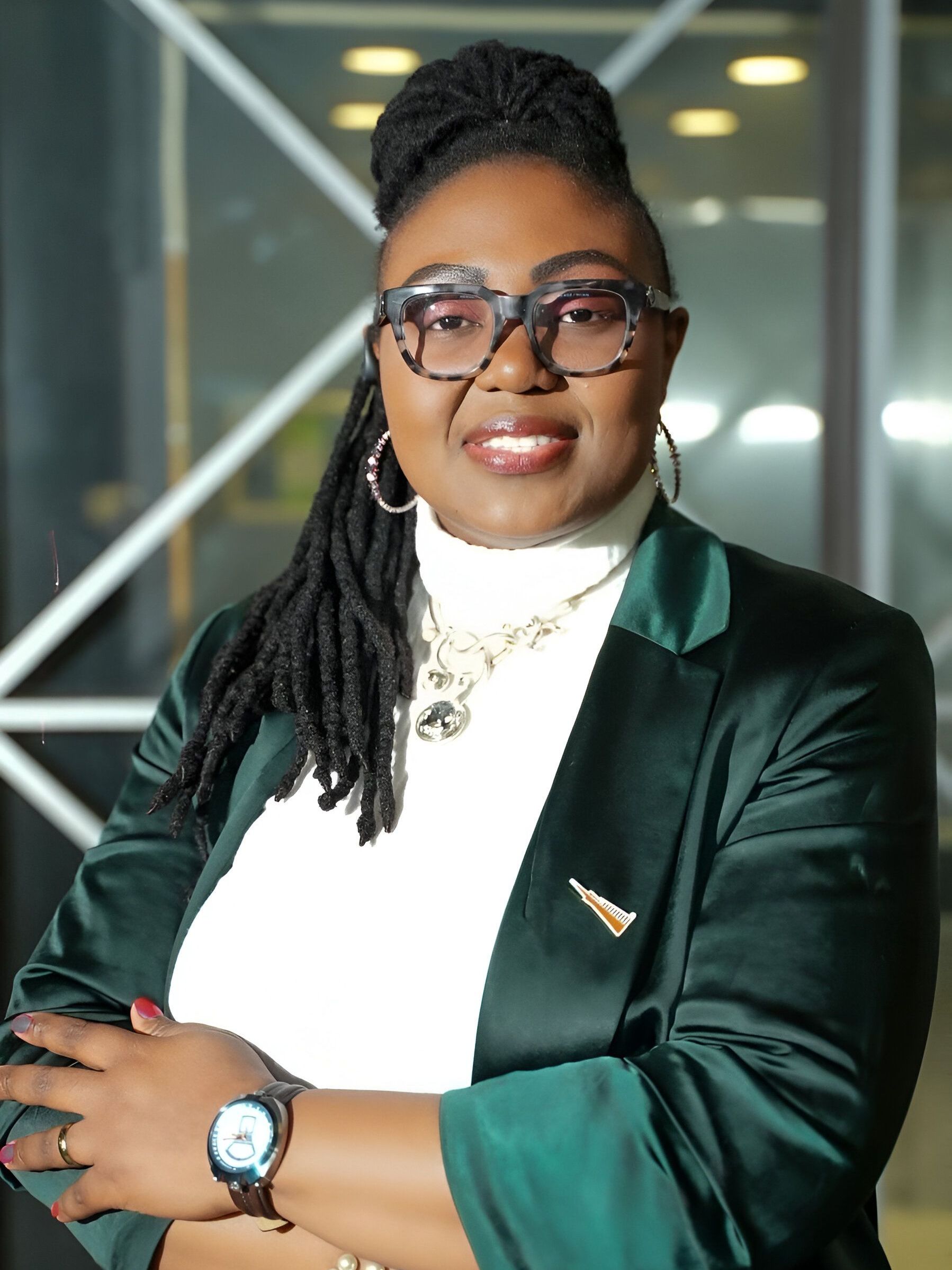 Dr Elodie Tendoh wearing glasses and a green jacket is posing for a picture.