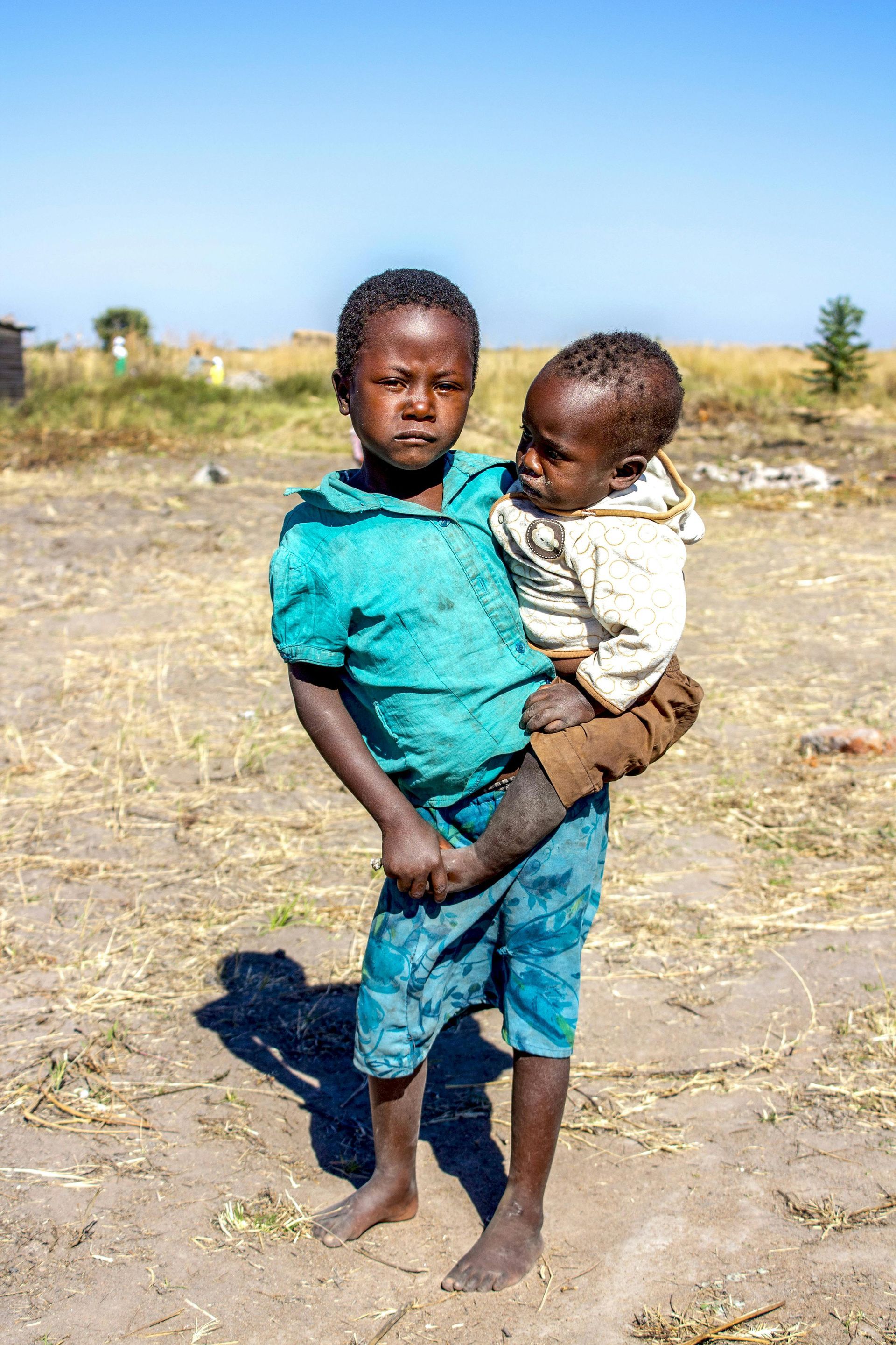 A young boy is holding a baby in his arms in a field.