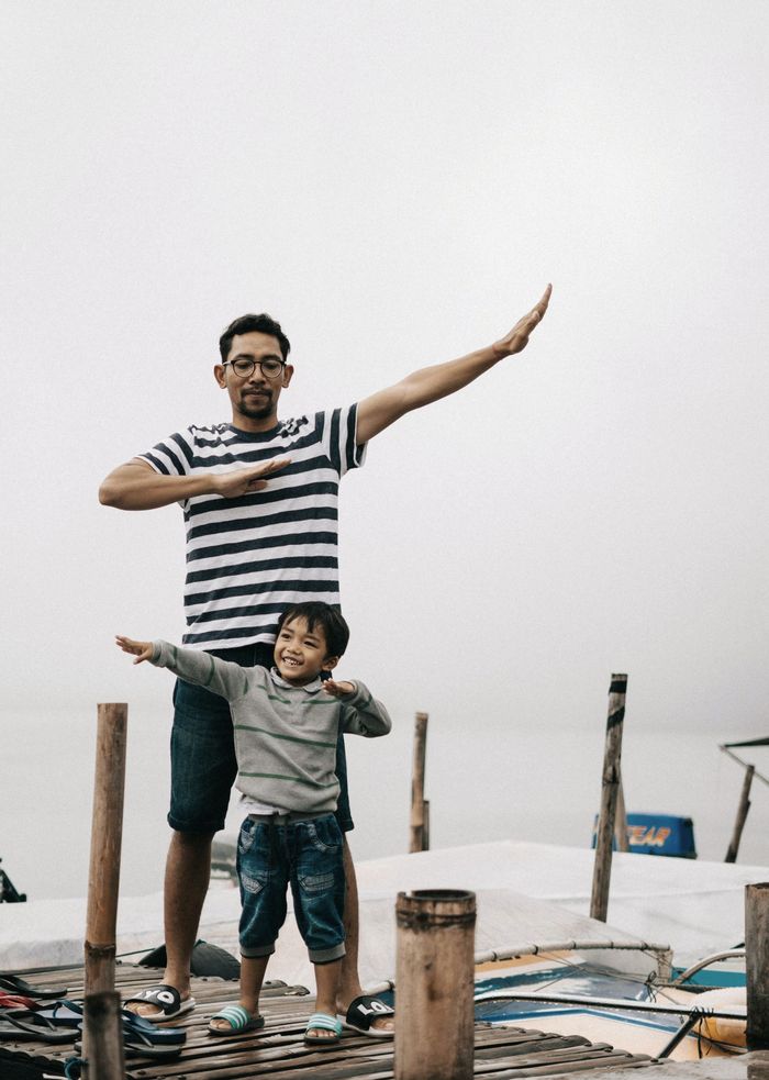 A man and a child are standing on a dock with their arms outstretched.