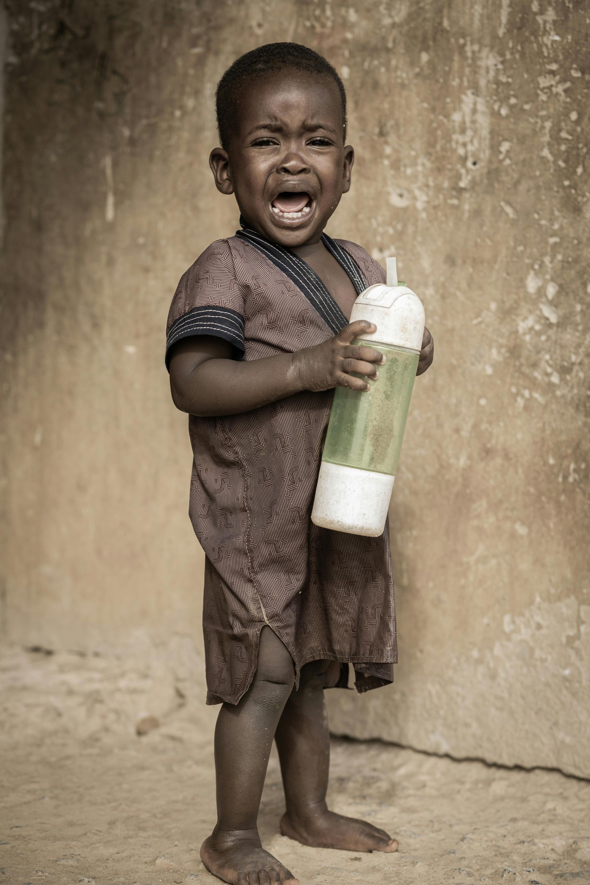A little boy is crying while holding a bottle of water.