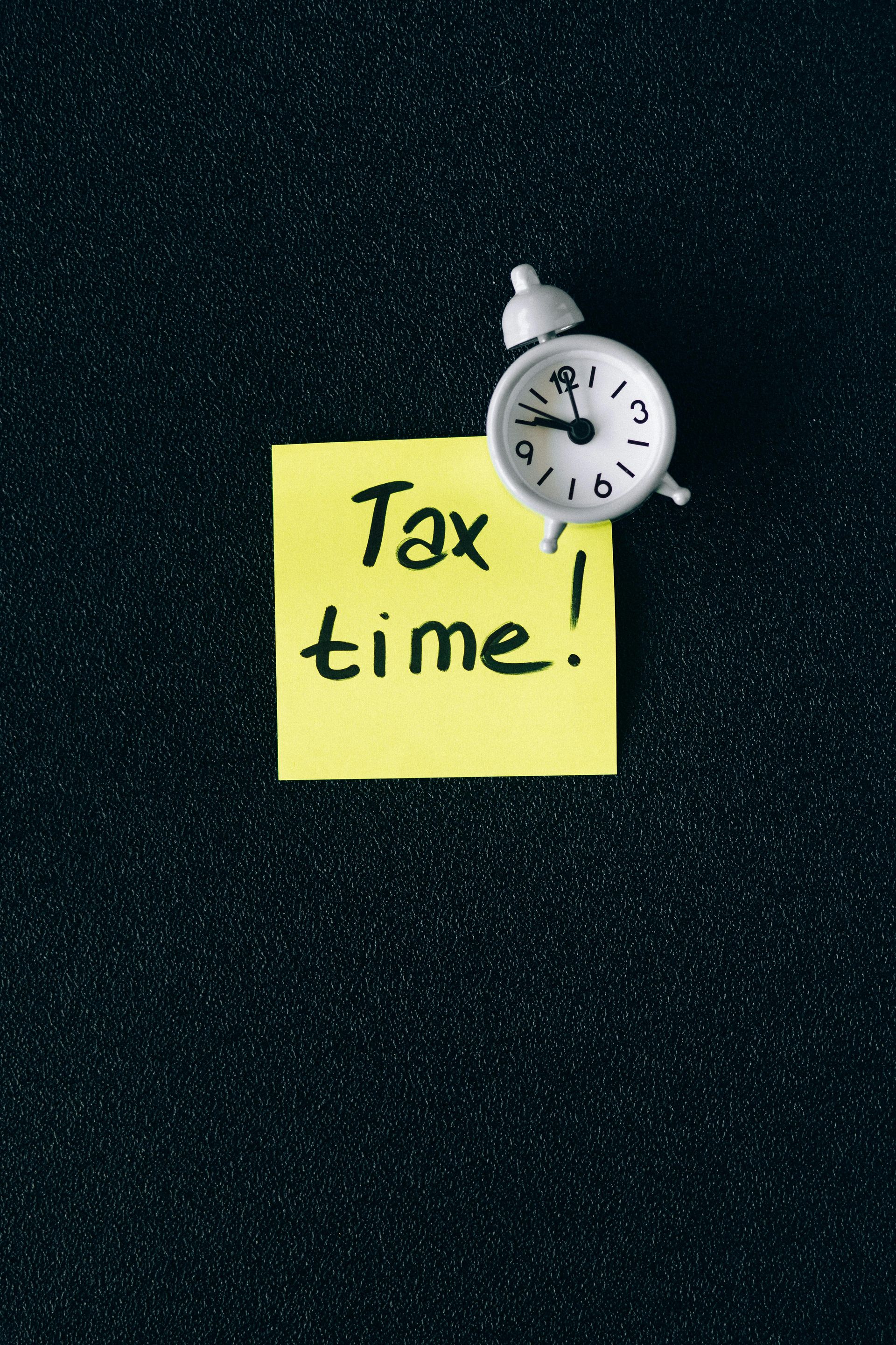 A yellow sticky note that says tax time next to an alarm clock