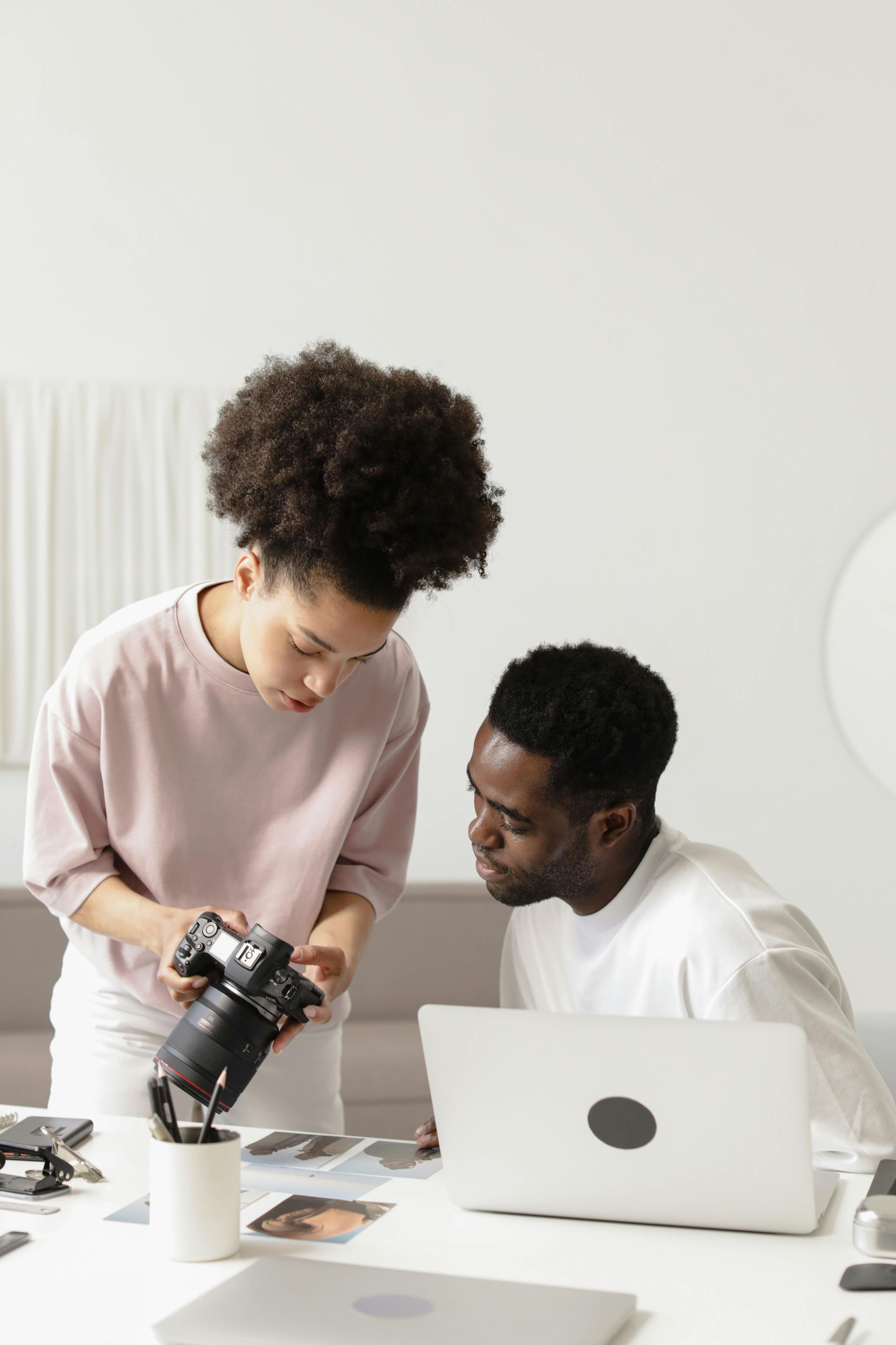 A man and a woman are looking at a camera while sitting at a table with a laptop.