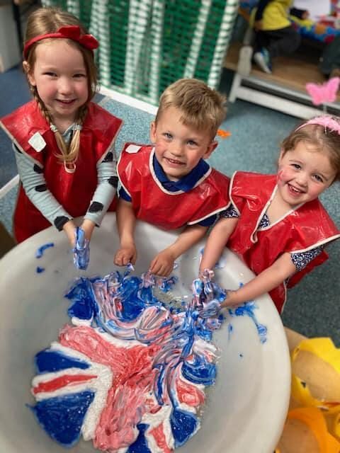 Three children are playing with red white and blue paint in a bowl.