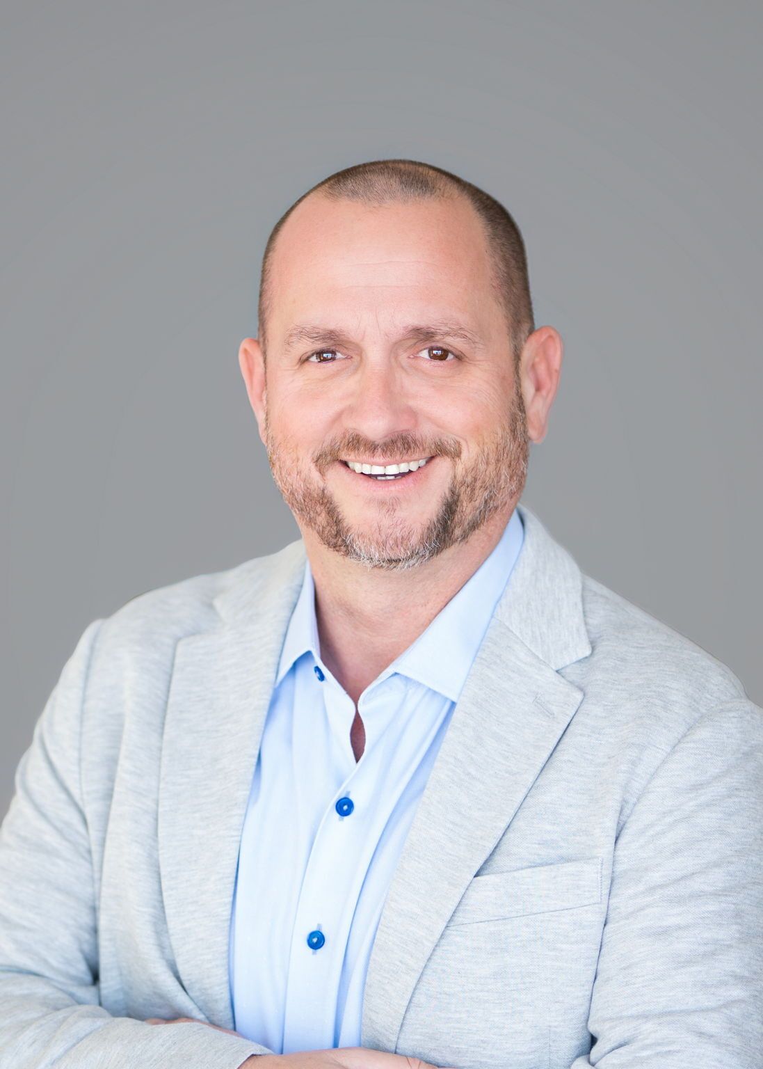 Man in blazer with arms crossed, smiling. Set against a white background with a blue border.