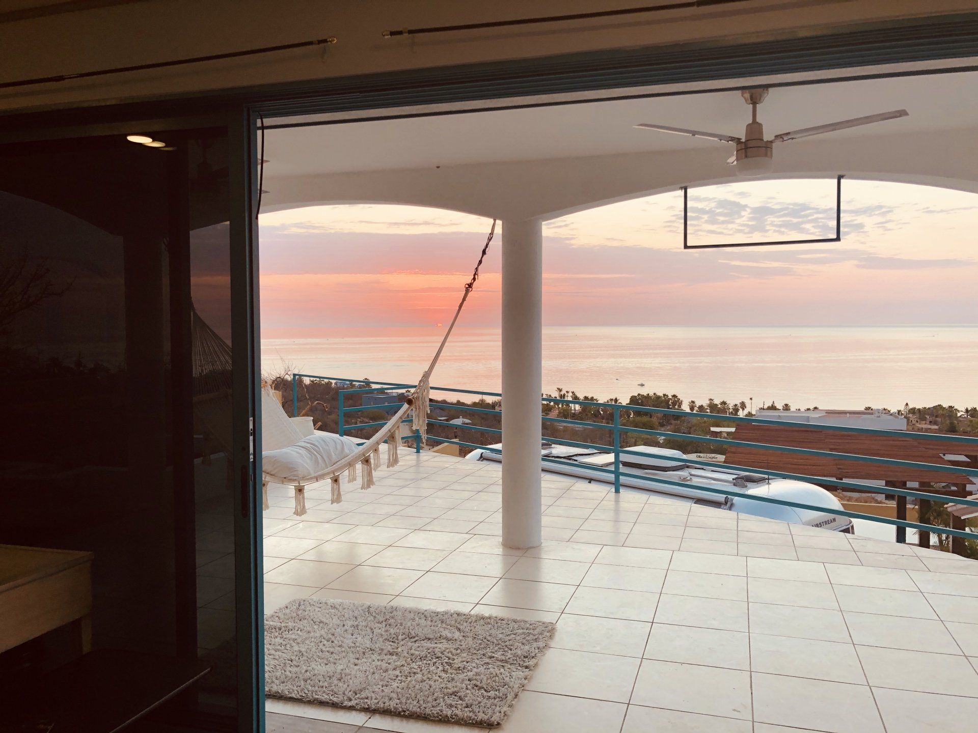 A balcony with a hammock and a view of the ocean at sunset.