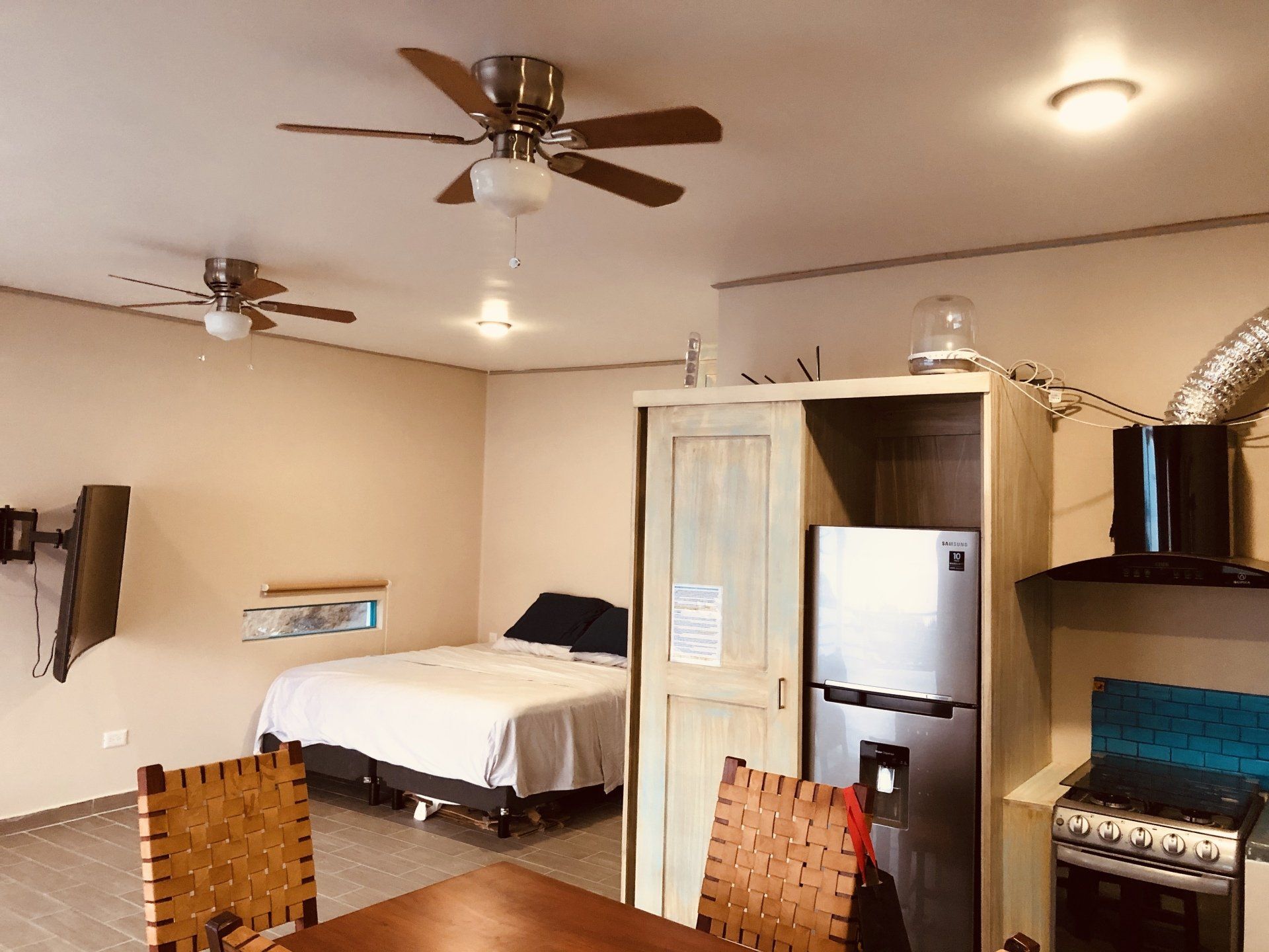 A bedroom with a ceiling fan , a refrigerator , a table and chairs.