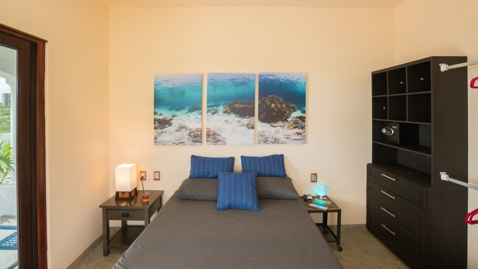 A bedroom with a bed , nightstand , dresser and paintings on the wall.