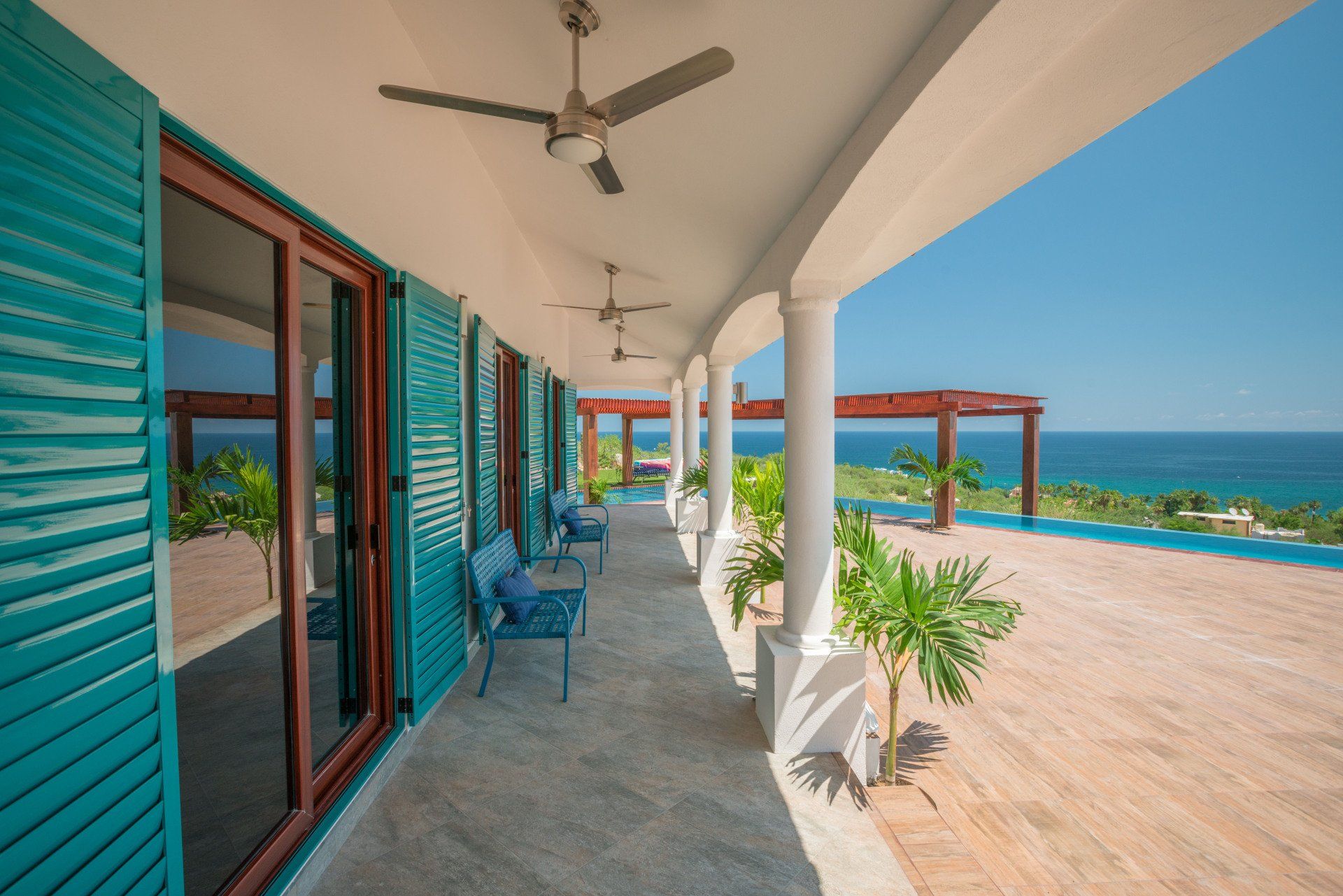 A balcony with blue shutters and a ceiling fan overlooking the ocean.