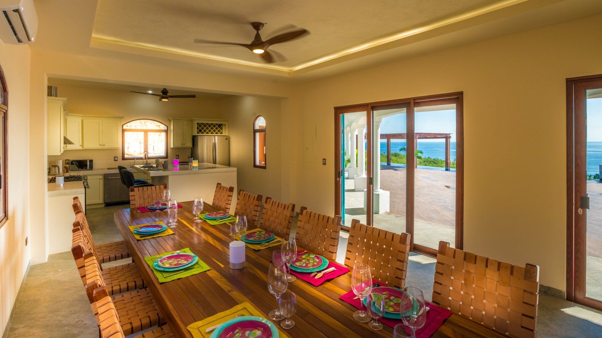 A dining room with a long wooden table and chairs and a ceiling fan.